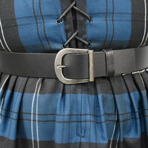 May include: A black leather belt with a silver buckle. The belt is worn over a blue and black plaid skirt.