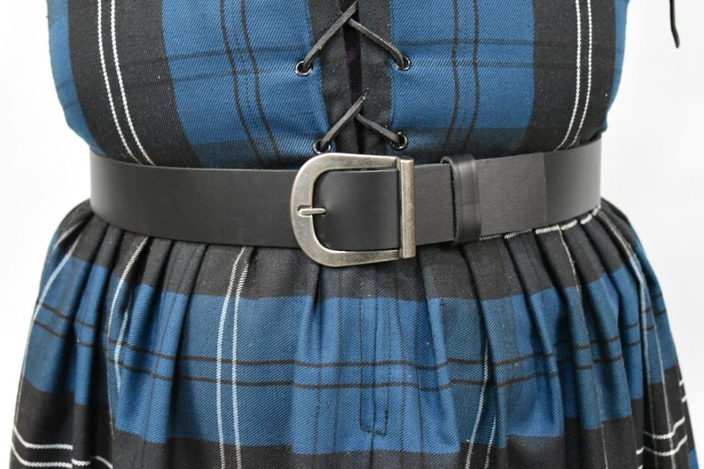 May include: A black leather belt with a silver buckle. The belt is worn over a blue and black plaid skirt.