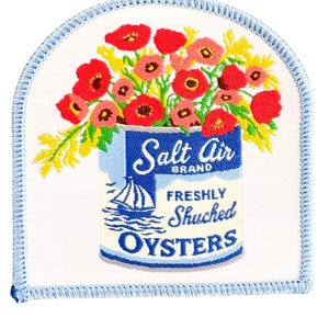 May include: Embroidered patch featuring a blue can labeled "Salt Air Brand Freshly Shucked Oysters" with a sailboat illustration. The can is overflowing with red, pink, and yellow flowers, set against a white background with a blue border.