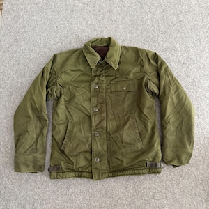 May include: Olive green jacket with a button-up front, two front pockets, and a brown collar. The jacket has a quilted lining and adjustable straps at the waist. A classic outerwear piece.