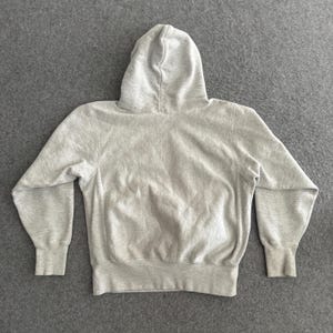 May include: A light gray hoodie with a hood, long sleeves, and ribbed cuffs and hem. The sweatshirt is made of a soft, comfortable material and is laid flat on a gray surface. The hoodie is a casual garment.
