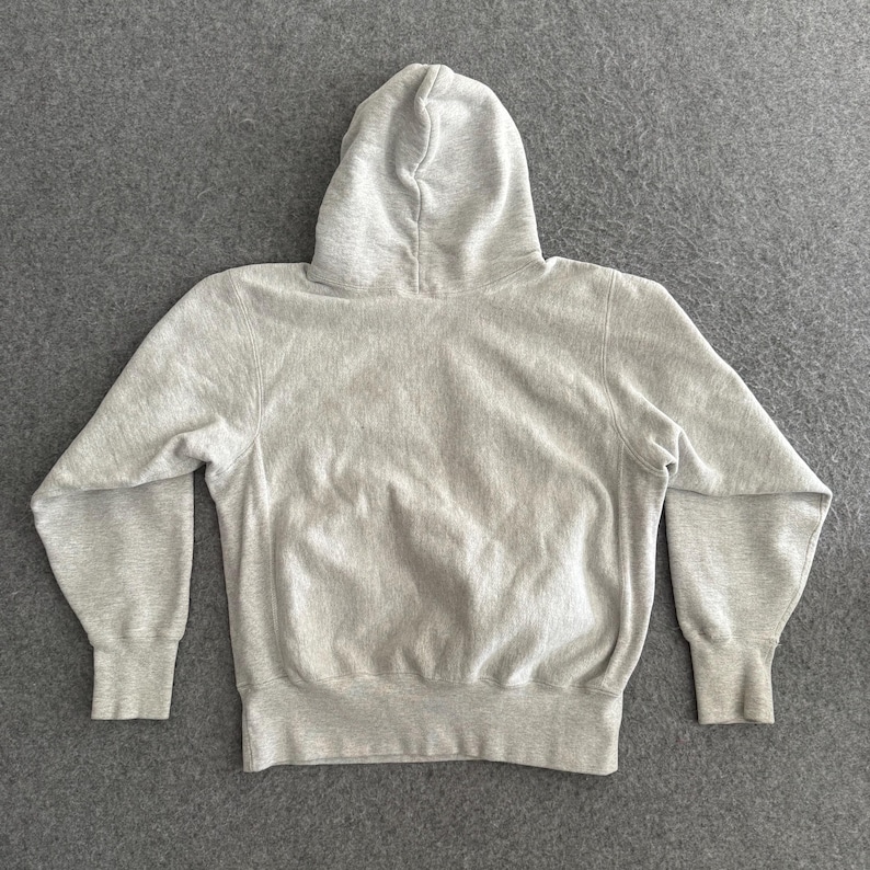 May include: A light gray hoodie with a hood, long sleeves, and ribbed cuffs and hem. The sweatshirt is made of a soft, comfortable material and is laid flat on a gray surface. The hoodie is a casual garment.
