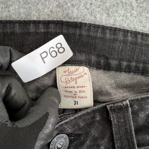 Pu&ograve; includere: Primo piano di jeans True Religion neri. I jeans hanno un'etichetta taglia 31 e un'etichetta del marchio che recita "Made in USA of imported fabric". &Egrave; visibile anche un'etichetta bianca con "P68".