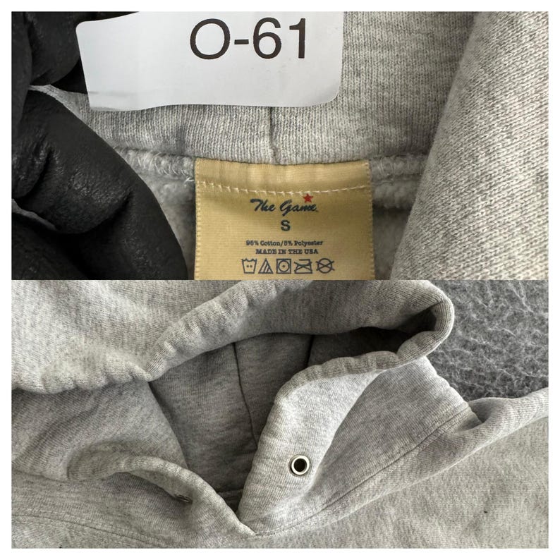 May include: Close-up of a gray hoodie with a drawstring hood. The tag reads "The Game" and "S". The hoodie is made of 90% cotton and 10% polyester. The tag also includes washing instructions and "MADE IN THE USA".