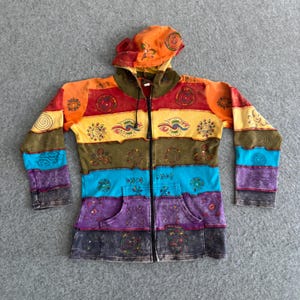 May include: A long-sleeve zip-up hoodie featuring horizontal color-blocked panels in orange, red, yellow, olive green, bright blue, purple, and charcoal gray. The garment is decorated with various embroidered circular and spiral motifs.