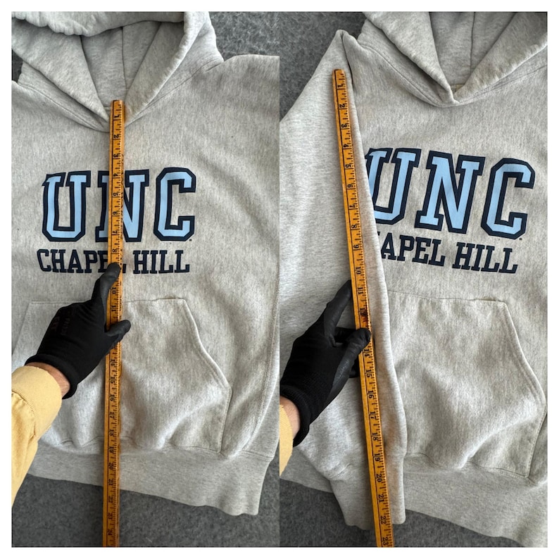 May include: A light gray hoodie with a front pocket and a hood. The hoodie features the text "UNC CHAPEL HILL" in blue and white. A measuring tape is held up to the hoodie.