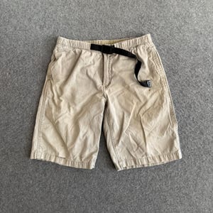 May include: Beige shorts with a black belt. The shorts feature an elasticated waistband and pockets. The shorts are made of a sturdy material and are suitable for casual wear.