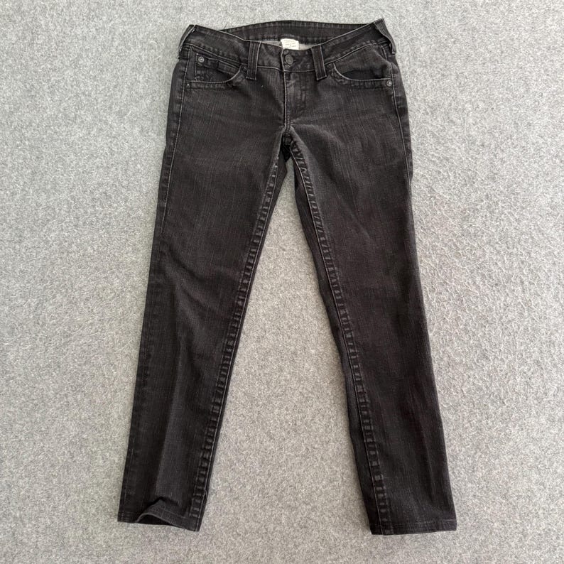 Pu&ograve; includere: Un paio di jeans neri. I jeans hanno un classico design a cinque tasche, una chiusura con bottone e cerniera e sono realizzati in denim scuro. Le cuciture sono di un colore a contrasto e i jeans sembrano essere in buone condizioni.