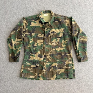 May include: A camouflage military jacket with long sleeves and several pockets. The jacket has the text "USMC" on the chest. The colour scheme includes shades of green, brown, and tan.