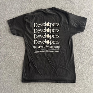 May include: A black short-sleeve t-shirt featuring white text on the back that reads Developers, Developers, Developers, Developers, We love this company!, and Apple Student Developers 2002, with the Apple logo replacing the letter o in each word.