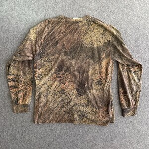 May include: Long-sleeved shirt with a camouflage pattern in shades of brown, tan, and green. The shirt has a crew neck and is made of a soft, possibly cotton, material. The camouflage design is detailed and covers the entire shirt.