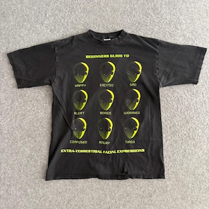 May include: Black t-shirt with a graphic featuring alien faces expressing different emotions. The text reads "BEGINNERS GUIDE TO EXTRA-TERRESTRIAL FACIAL EXPRESSIONS" with labels like "HAPPY," "SAD," and "ANGRY."