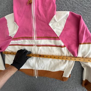 Op de afbeelding: Een roze, witte en bruine hoodie met ritssluiting. De sweatshirt heeft een witte rits, bruine geribde manchetten en een wit en bruin gestreept ontwerp over de borst. De borstbreedte is ongeveer 61 cm.