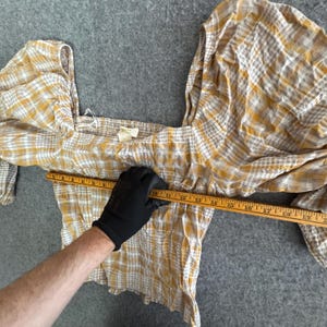May include: A yellow, white, and grey plaid crop top with a square neckline and puffed sleeves. The top is being measured with a wooden ruler. The top is approximately 35.5 cm wide.