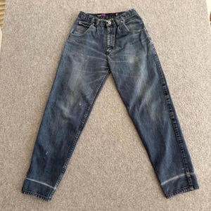May include: Blue denim jeans with a faded wash and a straight leg cut. The jeans have a button and zipper closure, front and back pockets, and a folded hem at the ankles. The denim has some light distressing.