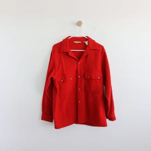 May include: A red long-sleeved button-up shirt with two large pockets on the front.