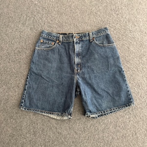 May include: A pair of medium-wash blue denim shorts featuring a classic five-pocket design, a button fly closure, copper-toned metal rivets, and visible stitching along the seams. The shorts have a straight-leg cut and a standard waistband.