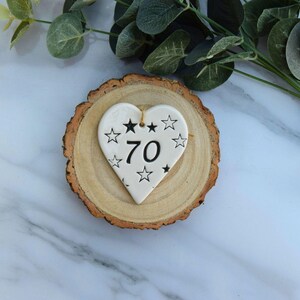 May include: White ceramic heart-shaped ornament with black stars and the number 70 on a wooden base.