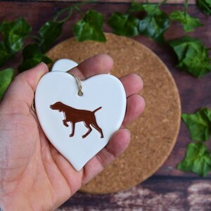 May include: White ceramic heart-shaped ornament featuring a brown silhouette of a German Shorthaired Pointer dog.