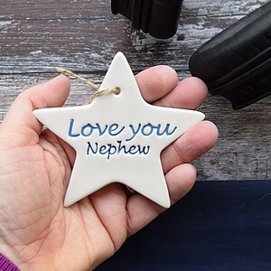 May include: White ceramic star ornament with blue lettering that reads "Love you Nephew".