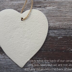 May include: A heart-shaped off-white ceramic ornament with a textured surface and a hole at the top for hanging. A piece of brown twine is threaded through the hole. The text reads: This is what the back of our ceramics look like, sorry but we are not able to add any detail onto the back of our items.