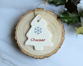 May include: White ceramic Christmas tree ornament with a blue snowflake and the word "Chwaer" in red lettering.