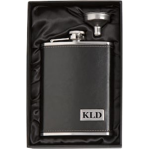 May include: Black leather-wrapped flask with a silver top and funnel, in a black velvet-lined box. The flask has a silver plate with the initials "KLD" engraved on it.