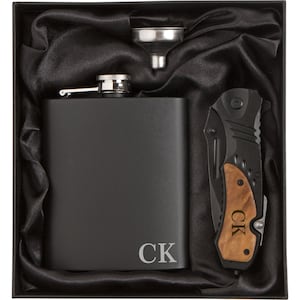 May include: A black gift box with a black flask, a funnel, and a pocket knife with a wood handle. The flask and knife are engraved with the initials "CK".
