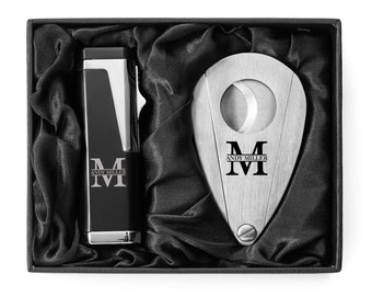 May include: A black gift box with a silver cigar cutter and lighter. The cutter and lighter are engraved with the letter "M" and the name "Andy Miller".