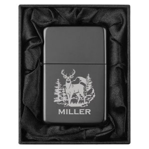 May include: A black lighter with a deer and forest scene engraved on the front. The lighter is in a black gift box with a satin lining. The name "MILLER" is engraved below the scene.