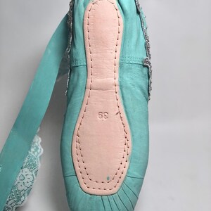 May include: A pair of turquoise ballet shoes with a pink leather insole and a white lace ribbon. The shoes have a size 36 printed on the insole.