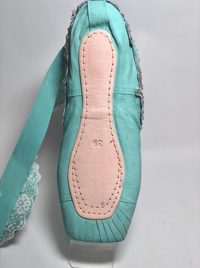 May include: A pair of turquoise ballet shoes with a pink leather insole and a white lace ribbon. The shoes have a size 36 printed on the insole.