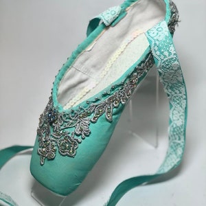May include: A pair of turquoise ballet shoes with silver and white lace embellishments and rhinestones.