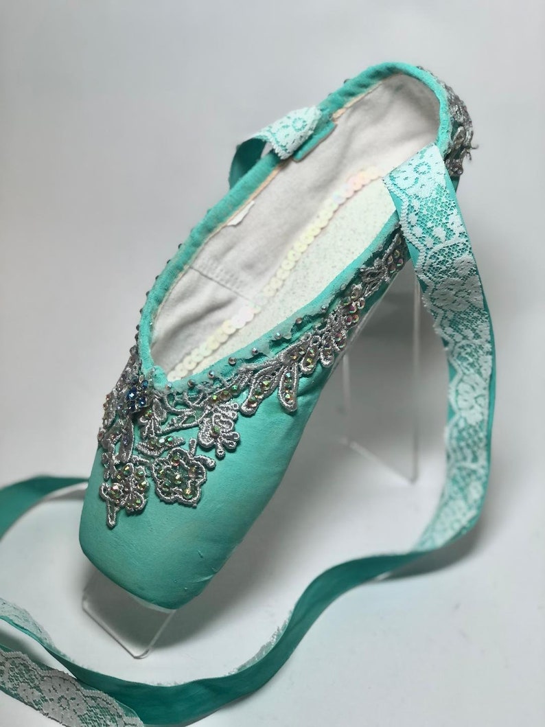 May include: A pair of turquoise ballet shoes with silver and white lace embellishments and rhinestones.