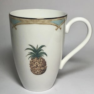 May include: White ceramic mug with a gold rim and a blue and brown pineapple design.