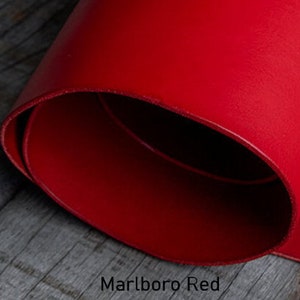 Puede incluir: Un trozo de cuero rojo enrollado, con el texto "Marlboro Red" en la parte inferior. El cuero es de un color s&oacute;lido y vibrante, y los bordes son lisos. El fondo es una superficie de madera.