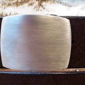 Könnte beinhalten: Ein brauner Ledergürtel mit einer silbernen Schnalle. Die Schnalle ist einfach rechteckig und hat eine gebürstete Oberfläche.