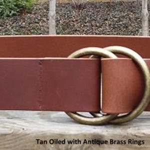 Puede incluir: Cintur&oacute;n de cuero curtido de color canela con anillos de lat&oacute;n antiguo. El cintur&oacute;n tiene una hebilla de doble anillo. El texto "Tan Oiled with Antique Brass Rings" es visible en la parte inferior de la imagen. Dise&ntilde;o cl&aacute;sico.