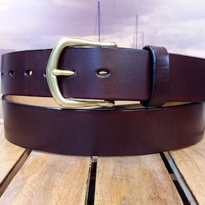 May include: A brown leather belt with a brass buckle. The belt is folded in half and the buckle is visible.