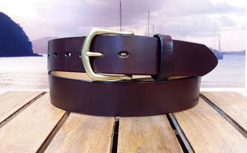 May include: A brown leather belt with a brass buckle. The belt is folded in half and the buckle is visible.