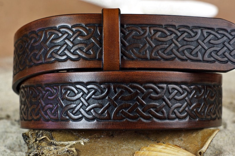May include: A brown leather belt with a Celtic knot design. The belt is embossed with a dark brown pattern.