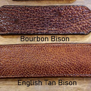May include: Two rectangular leather strips with rounded ends and a textured surface. The top strip is dark brown with the text Bourbon Bison below it. The bottom strip is a lighter tan color with the text English Tan Bison below it.