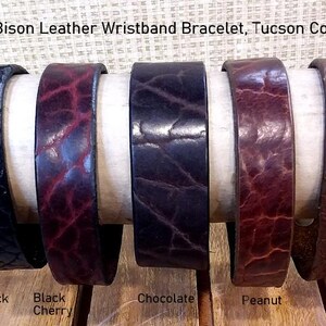 May include: Five Bison Leather Wristband Bracelets in Tucson Colors. The bracelets feature a textured grain and are available in black, black cherry, chocolate, peanut, and cognac. The text Bison Leather Wristband Bracelet, Tucson Colors is visible.
