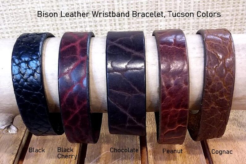 May include: Five Bison Leather Wristband Bracelets in Tucson Colors. The bracelets feature a textured grain and are available in black, black cherry, chocolate, peanut, and cognac. The text Bison Leather Wristband Bracelet, Tucson Colors is visible.
