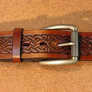 May include: A brown leather belt with a silver buckle featuring a Celtic knot design.
