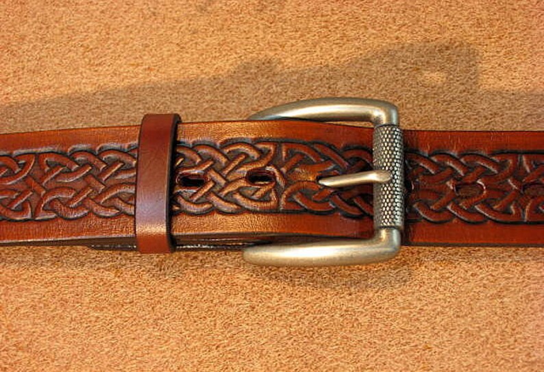 May include: A brown leather belt with a silver buckle featuring a Celtic knot design.