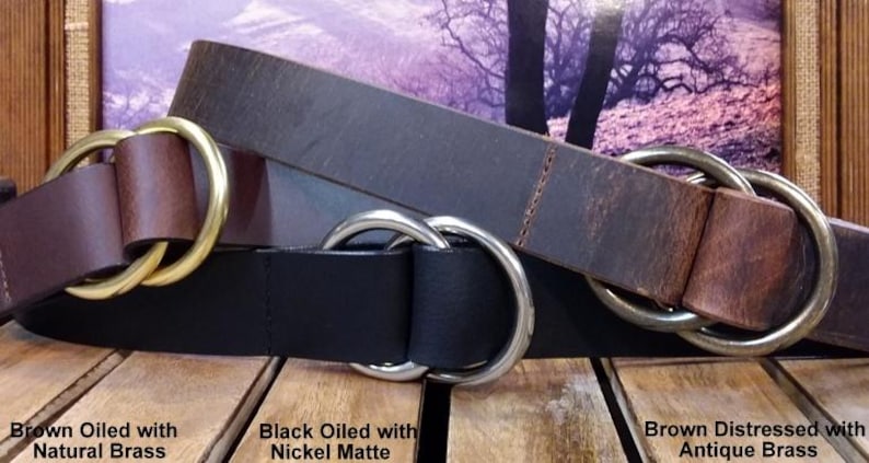 Puede incluir: Tres cinturones de cuero en marr&oacute;n y negro, cada uno con una hebilla de doble anilla. Los cinturones est&aacute;n etiquetados: "Brown Oiled with Natural Brass", "Black Oiled with Nickel Matte" y "Brown Distressed with Antique Brass".