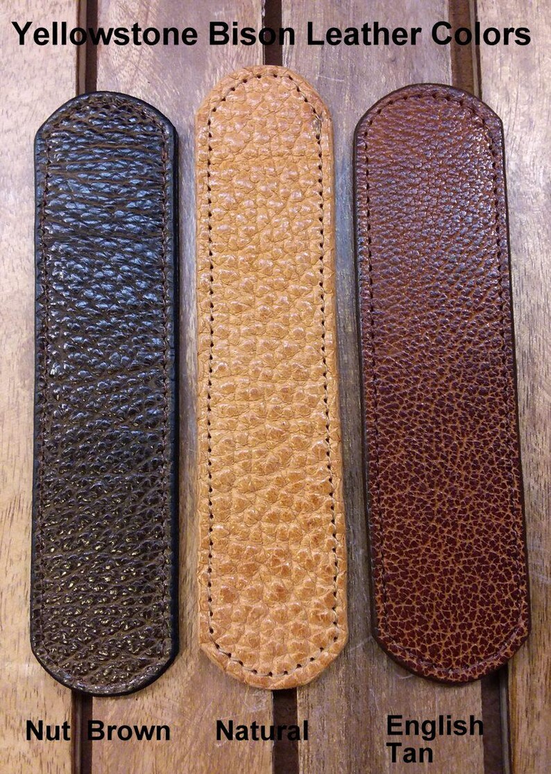 May include: Three rectangular bison leather strips with rounded ends and stitched edges, labeled Yellowstone Bison Leather Colors. The colors are Nut Brown, Natural, and English Tan, each featuring a distinct pebbled texture and grain.
