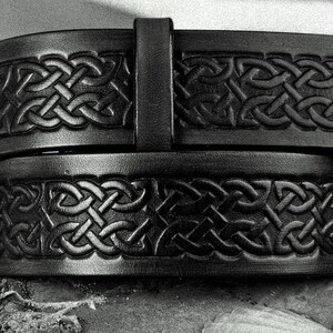 May include: A black leather belt with a Celtic knot design. The belt is folded in half, showing the intricate details of the knotwork.