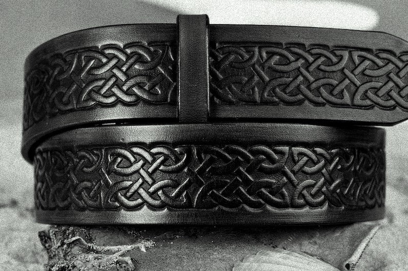 May include: A black leather belt with a Celtic knot design. The belt is folded in half, showing the intricate details of the knotwork.